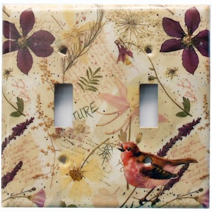 May include: A double light switch cover with a cream background featuring a pressed flower design. The design includes a pink flower, purple flowers, a bird, and the word "nature".