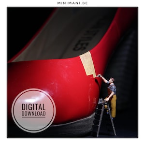 Op de afbeelding: Een felrode schoen met hoge hak met een miniatuurfiguurtje van een arbeider in een gele tuinbroek op een ladder, die een gouden streep op de zijkant schildert. De tekst MINIMANI.BE staat bovenaan en een ronde DIGITAL DOWNLOAD-badge is zichtbaar.