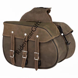 May include: A brown leather motorcycle saddlebag featuring three vertical straps with silver-toned metal buckles and matching studs. The bag has a curved flap design with black piping along the edges and the text RiderGearGifts printed diagonally.