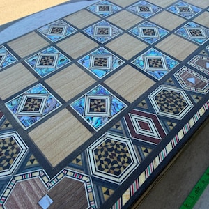 May include: A rectangular wooden game board featuring an intricate marquetry pattern of light wood squares alternating with decorative diamond-shaped inlays of iridescent abalone shell and dark wood geometric star motifs, bordered by a complex mosaic edge.