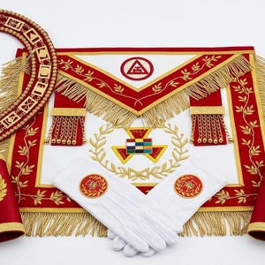 May include: A collection of Masonic regalia, including a red and white apron with gold fringe, a collar, cuffs, and white gloves. The items feature gold embroidery and various geometric symbols.