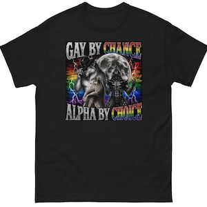 May include: A black t-shirt featuring a graphic print of two wolves, one wearing a cowboy hat, standing before a full moon and lightning bolts. The text "GAY BY CHANCE ALPHA BY CHOICE" is printed in rainbow-colored letters above and below the wolves.