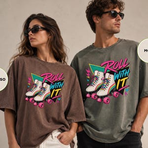 A woman wearing a brown t-shirt with a graphic of roller skates and the text "Roll with it" and a man wearing a gray t-shirt with the text "MOSS" and a graphic of roller skates.