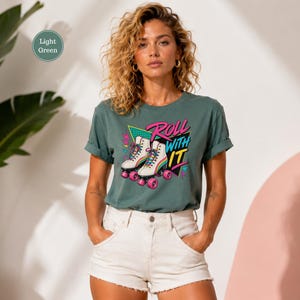 A woman wearing a green t-shirt with a graphic of rollerblades and the text "Roll with it" stands in front of a pink wall.