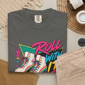 a variety of items, including a black t-shirt with a graphic design, a hat, a wooden box, a notebook, a pen, a cup, a bowl, and some dried flowers.