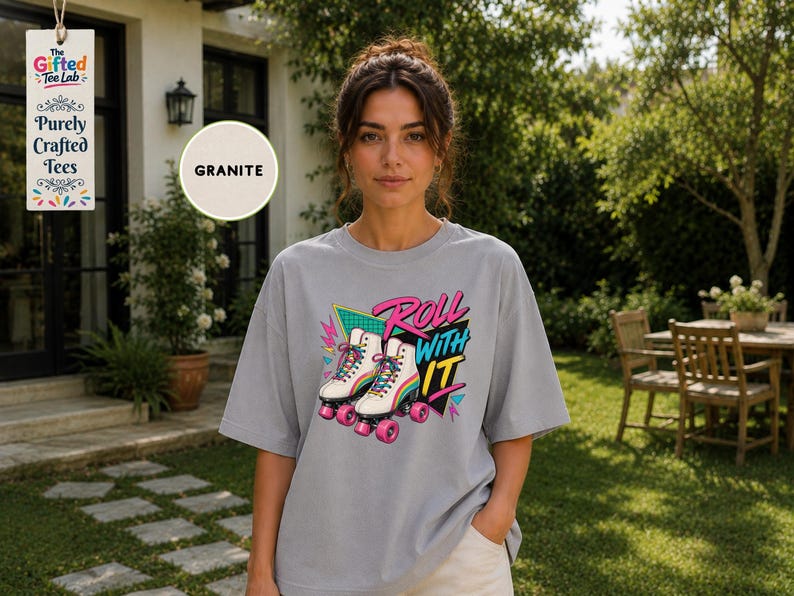A woman wearing a gray t-shirt with a graphic design of rollerblades and the text "Roll with it" stands in front of a house with a sign that says "Gifted Tee Lab".