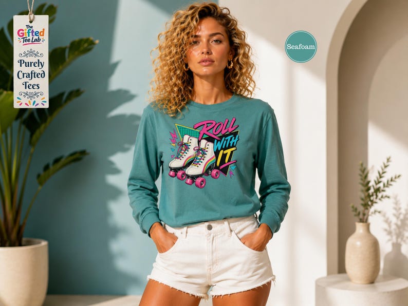 A woman with curly hair wearing a teal long-sleeved shirt with a graphic of roller skates and the text "Roll with it" stands in a room with a potted plant and a vase.