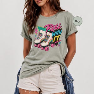 A woman wearing a gray t-shirt with a graphic design of roller skates and the text "Roll with it" printed on it.