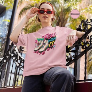 A woman wearing a pink t-shirt with a graphic of roller skates and the text "Roll with it" is sitting on a chair.