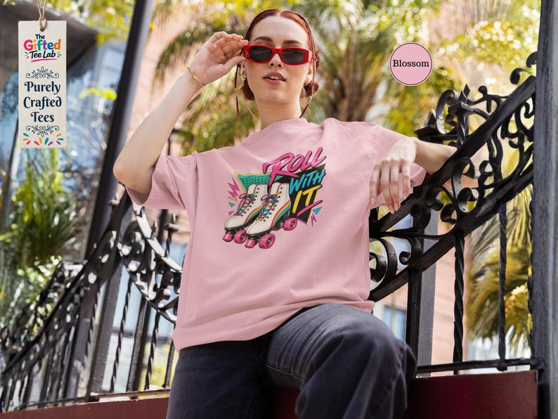 A woman wearing a pink t-shirt with a graphic of roller skates and the text "Roll with it" is sitting on a chair.