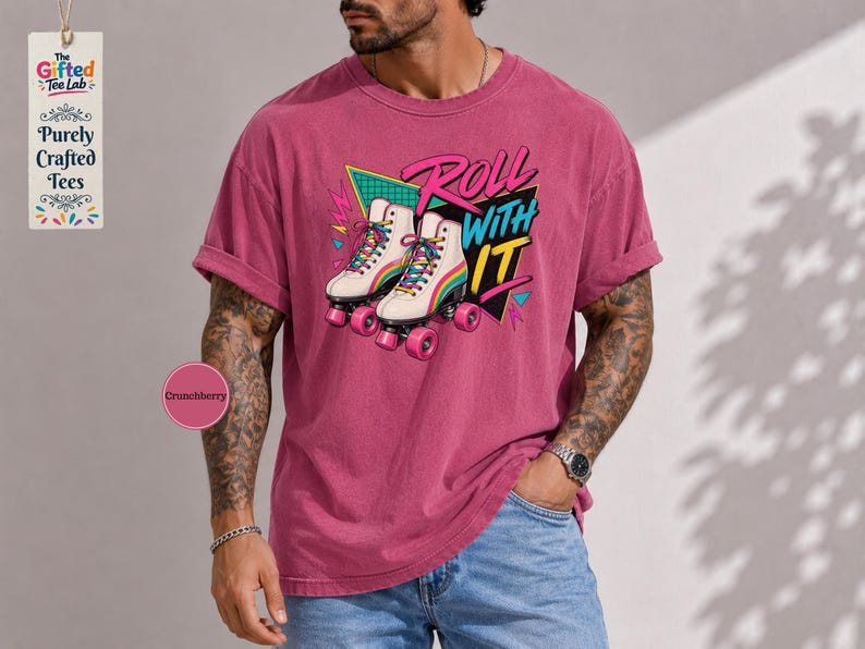 A man wearing a pink t-shirt with a graphic of roller skates and the text "Roll with it" is standing in front of a gray wall.