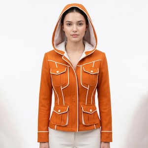 May include: A burnt orange hooded jacket featuring a white interior lining and white piping trim along the seams. The jacket includes four front pockets with button closures and a structured fit, paired with plain white trousers.