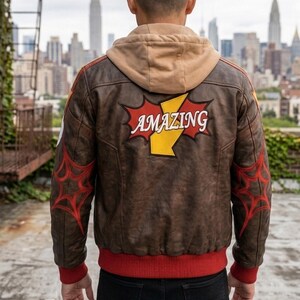 Rear view of a man on a city rooftop wearing Marvel Rivals Inspired Spider-Man Bomber Leather Jacket with Hoodie with red web designs on the sleeves and a large red and yellow patch reading "AMAZING" on the back.