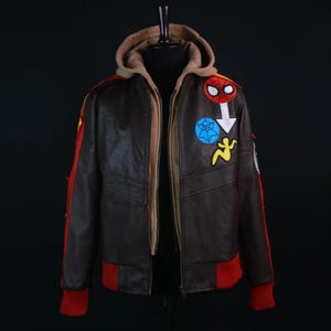 Marvel Rivals Inspired Spider-Man Bomber Leather Jacket with Hoodie. The jacket features vibrant embroidered superhero patches on the left chest, including a Spider-Man mask, a blue web symbol, and a yellow figure silhouette. It has red rib-knit cuffs and a matching red waistband.