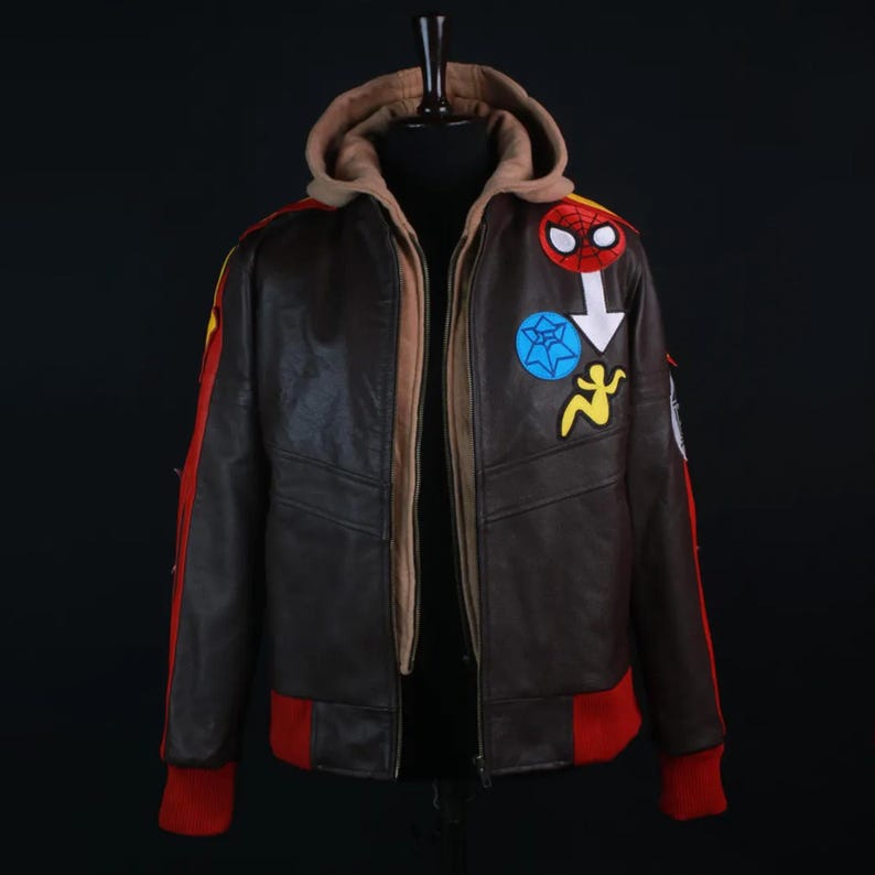 Marvel Rivals Inspired Spider-Man Bomber Leather Jacket with Hoodie. The jacket features vibrant embroidered superhero patches on the left chest, including a Spider-Man mask, a blue web symbol, and a yellow figure silhouette. It has red rib-knit cuffs and a matching red waistband.