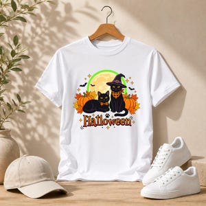 A graphic design featuring two black cats, one wearing a purple witch hat and orange bandana, sitting among pumpkins and autumn leaves under a full moon with the word Halloween below.