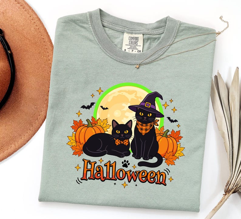 A graphic design featuring two black cats, one wearing a purple witch hat and orange bandana, sitting among pumpkins and autumn leaves under a full moon with the word Halloween below.
