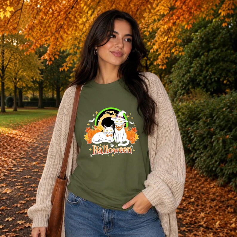 A graphic design featuring two black cats, one wearing a purple witch hat and orange bandana, sitting among pumpkins and autumn leaves under a full moon with the word Halloween below.