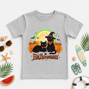 A graphic design featuring two black cats, one wearing a purple witch hat and orange bandana, sitting among pumpkins and autumn leaves under a full moon with the word Halloween below.