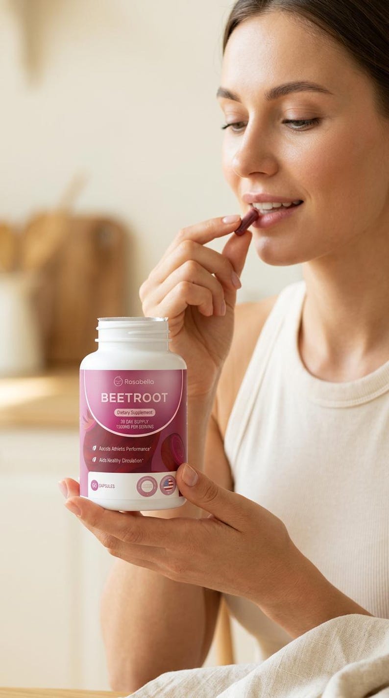 May include: A white bottle of Rosabella Beetroot dietary supplement with a pink label. The label includes text about athletic performance and healthy circulation. A person is holding a capsule from the bottle.