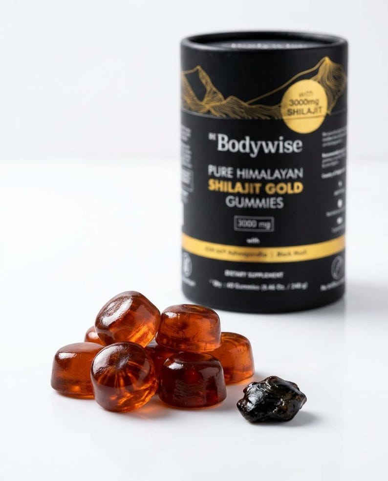 Pode incluir: Um recipiente cil&iacute;ndrico preto com gr&aacute;ficos de montanhas douradas e texto para "Bodywise Pure Himalayan Shilajit Gold Gummies" est&aacute; ao lado de uma pilha de gomas de cor &acirc;mbar e um peda&ccedil;o escuro de forma irregular.