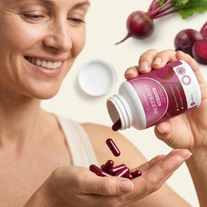 May include: A woman pouring dark red beetroot capsules from a white bottle into her hand. The bottle has a pink label with the word "BEETROOT" and a beetroot graphic. Fresh beetroots with green leaves are in the background.