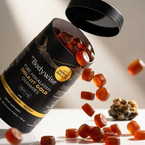 Pode incluir: Um recipiente cil&iacute;ndrico preto de Bodywise Pure Himalayan Shilajit Gold Gummies com a tampa aberta, e gomas a sair. O recipiente tem letras douradas e um desenho de montanha dourada. As gomas s&atilde;o de cor &acirc;mbar transl&uacute;cida.