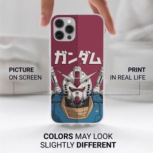 May include: A smartphone case featuring a graphic illustration of a Gundam robot head in white, blue, and tan colors against a dark red background. The Japanese text "ガンダム" is printed above the robot. The case has a camera cutout at the top.