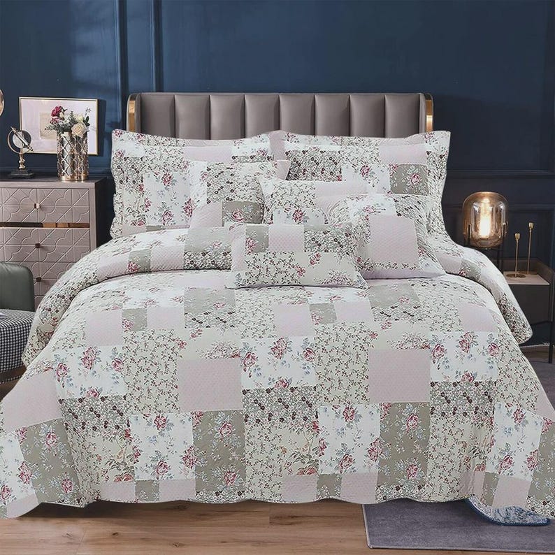 May include: A patchwork quilt and matching pillow shams featuring a repeating pattern of soft pink roses, muted green foliage, and solid light pink squares. The bedding set displays a coordinated floral design across the entire surface area.