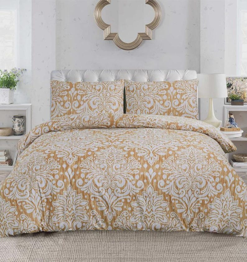 May include: A bedding set featuring a mustard yellow and white damask pattern. The set includes a duvet cover and two matching pillow shams, all displaying a repeating ornate floral motif across the fabric surface, creating a cohesive look.