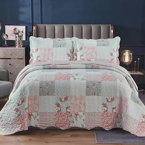 May include: A patchwork quilt and two matching pillow shams featuring a repeating pattern of soft pink and sage green floral prints, gingham checks, and subtle textures. The bedding set displays a quilted finish with a consistent color palette.