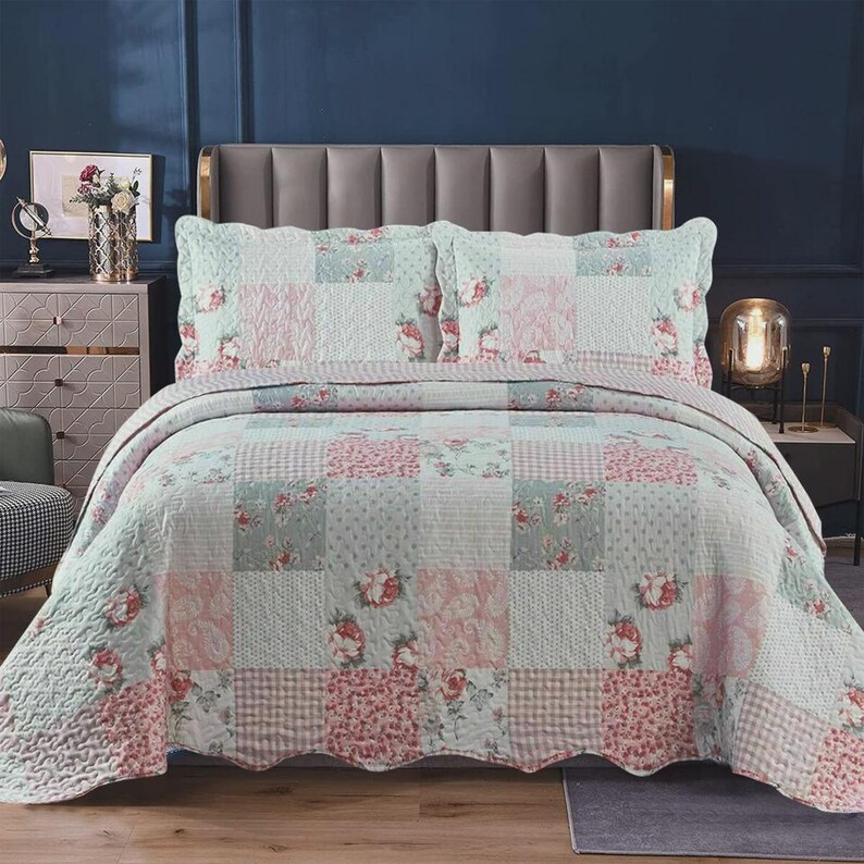 May include: A patchwork quilt and two matching pillow shams featuring a repeating pattern of soft pink and sage green floral prints, gingham checks, and subtle textures. The bedding set displays a quilted finish with a consistent color palette.