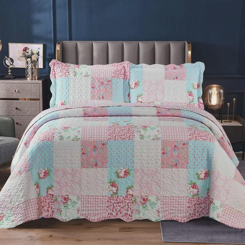 May include: A patchwork quilt and two matching pillow shams featuring a repeating pattern of pink roses, light blue floral prints, and pink and white gingham checks. The bedding set has a scalloped edge and a quilted texture throughout the fabric.