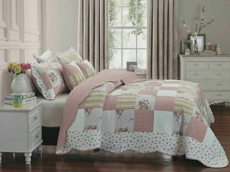 May include: A patchwork quilt and matching pillow shams featuring a repeating pattern of pink gingham, cream stripes, and floral prints. The bedding set has a scalloped edge and is displayed on a bed with white pillows and a white nightstand.