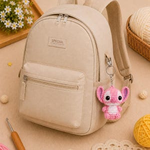 May include: Beige backpack with a front pocket and silver zippers. A small, pink and white crocheted Stitch keychain hangs from the side. The backpack has the word "SPECIAL" on the front.