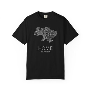 Könnte beinhalten: Schwarzes T-Shirt mit weißer Umrisszeichnung der ukrainischen Karte. Unter der Karte steht in Weiß das Wort "HOME", darunter "УКРАЇНА". Das T-Shirt hat kurze Ärmel und einen Rundhalsausschnitt.