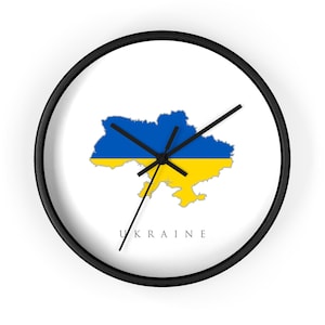 Könnte beinhalten: Eine runde Wanduhr mit schwarzem Rahmen und weißem Zifferblatt. In der Mitte befindet sich eine Karte der Ukraine in den blau-gelben Farben der Nationalflagge. Das Wort UKRAINE ist in schwarzen Großbuchstaben unter der Karte gedruckt. Drei schwarze Zeiger.
