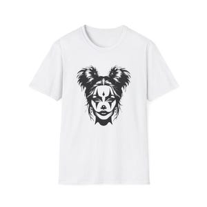 Könnte beinhalten: Ein weißes Kurzarm-T-Shirt mit einem zentrierten schwarzen Grafikdruck eines Gesichts mit Clown-Make-up, einschließlich Rautenformen um die Augen und einer dunklen Nase, sowie einer Frisur mit zwei hohen Knoten auf dem Kopf.