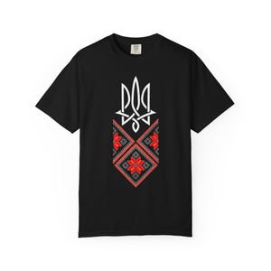 Könnte beinhalten: Schwarzes T-Shirt mit einem weißen Dreizack-Design und einem rot-schwarzen geometrischen Muster. Das Design ist eine stilisierte Darstellung eines Wappens. Das Shirt besteht aus einem weichen Material.