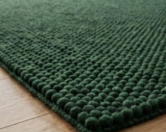 May include: A rectangular area rug in a deep forest green color, featuring a dense, textured surface composed of numerous small, uniform felted wool balls arranged in a tight grid pattern across the entire top side of the floor covering.