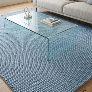 May include: A light blue area rug with a textured, bobble-knit surface featuring a repeating spherical pattern. The rectangular rug is positioned on a wooden floor and displays the text ArtResourceCarpet in the bottom right corner.
