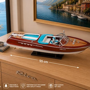 Op de afbeelding: Een model speedboot van 55 cm lang, voorzien van een gepolijste donkerhouten romp, een wit en turquoise interieur, een chromen voorruit en metalen dekdetails. Op de zijkant van de boot staat de tekst Aquarama en Riva in witte letters.