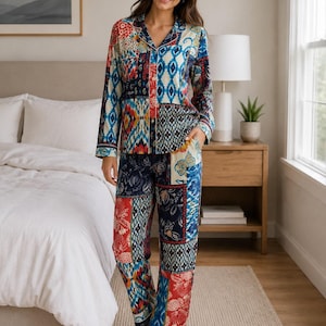 Pode incluir: Um conjunto de pijama de duas peças composto por uma camisa de manga comprida com botões e calças a condizer. O tecido apresenta um padrão de patchwork vibrante com vários desenhos geométricos, florais e ikat em tons de vermelho, azul, creme e azul-marinho.