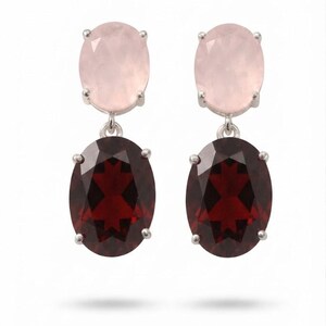 Puede incluir: Un par de pendientes colgantes con piedras de cuarzo rosa ovaladas en la parte superior, unidas mediante garras de plata a piedras de granate rojo oscuro ovaladas más grandes en la parte inferior. Las piedras están talladas y engastadas en plata.