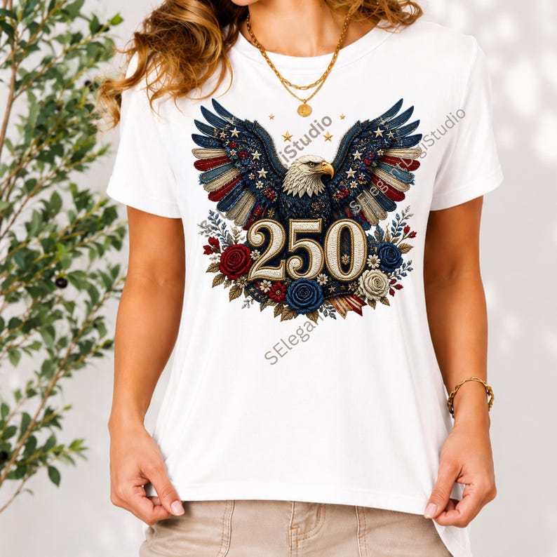 May include: A white short-sleeved t-shirt featuring a graphic of a bald eagle with wings spread, colored in red, white, and blue with star patterns. The number 250 is centered below the eagle, surrounded by red, white, and blue floral accents.