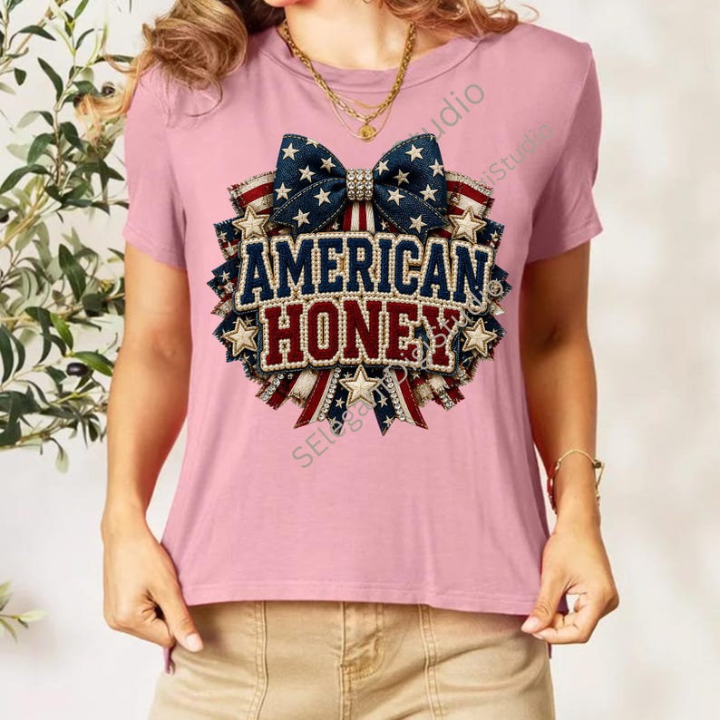 May include: A light pink short-sleeve t-shirt featuring a central graphic of a blue bow with white stars above the text AMERICAN HONEY in blue and red letters, surrounded by a circular patriotic ribbon design with red, white, and blue stripes.