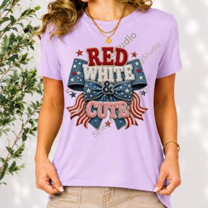 May include: A light purple short-sleeve t-shirt featuring a central graphic of a denim-textured bow with red, white, and blue stars and stripes. The text "RED WHITE & CUTE" is printed in a textured, layered font across the center of the bow.