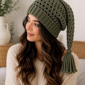 May include: An olive green crochet beanie featuring a ribbed brim, a textured open-stitch pattern throughout the crown, and a long, dangling tail that terminates in a thick, matching yarn tassel. The hat is crafted from solid olive green yarn.