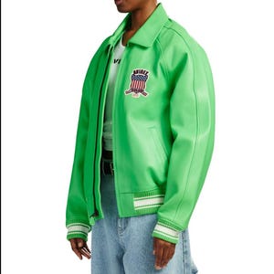 May include: A bright lime green bomber jacket featuring a classic collar, a front zipper closure, and ribbed cuffs and hem with white stripes. An embroidered patch on the chest displays the text AVIREX above a shield with a red, white, and blue flag.