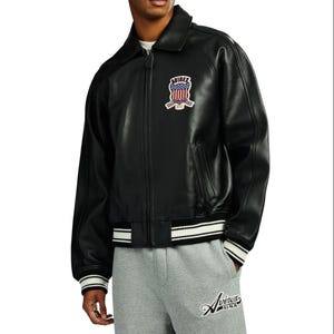 May include: A black leather jacket with a fold-down collar, a full-length front zipper, and ribbed cuffs and hem featuring white stripes. A patch on the chest displays the text AVIREX with an American flag graphic and the words ESTABLISHED 1975.